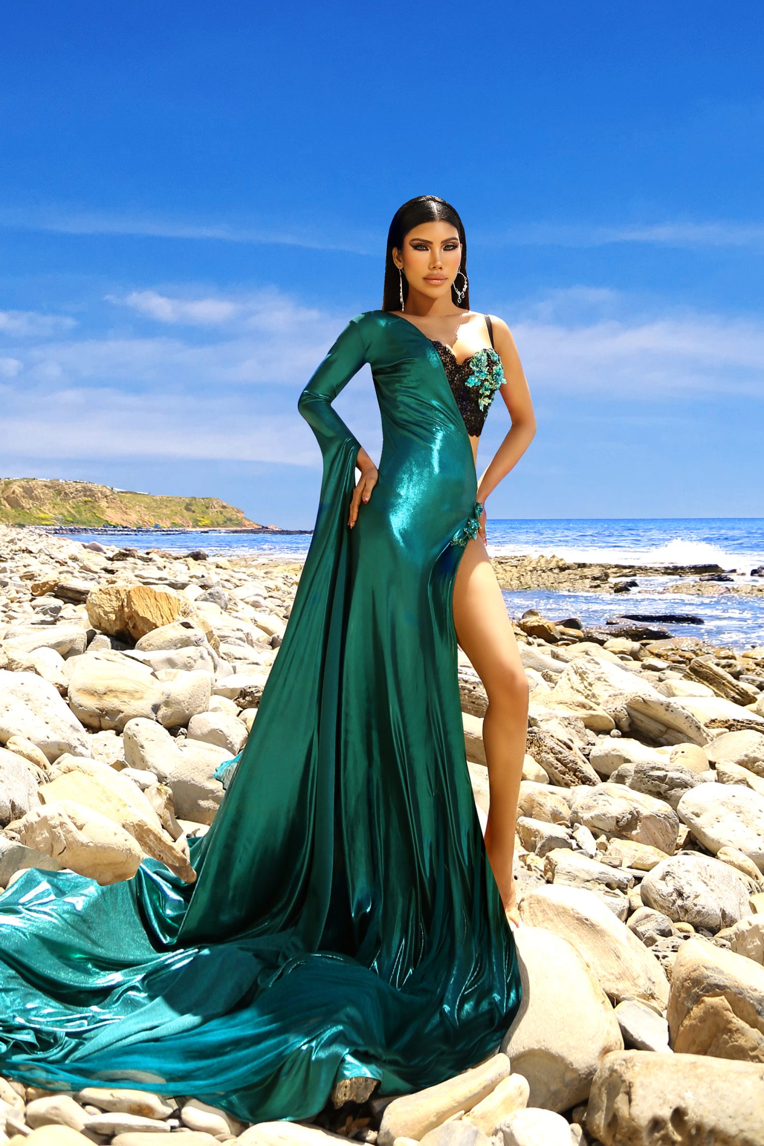 Two Piece Mermaid Gown The Shiny Sheer Senorita mermaid gown is a sartorial treasure that redefines elegance. This two piece marvel, with its form-fitting emerald green bodice and flowing black skirt, creates a silhouette that celebrates the female form. The mermaid cut of the gown flares at the knee, mimicking the graceful curves of oceanic tales, while the spandex material ensures a perfect fit that accentuates your natural grace. Long Sleeve One Shoulder Cape Draped over one shoulder, the long sleeve cape adds a touch of drama and sophistication to the ensemble. This floor-grazing element of design brings a regal air to the gown, its sheer fabric billowing like a banner of nobility. It is a modern nod to the capes of yesteryears, reimagined for the contemporary goddess. Crystal Beadwork The gown’s bodice is a canvas for the exquisite crystal beadwork that adorns it. Handcrafted with precision, the beads catch the light and twinkle like stars against the night sky. The intricate patterns formed by the crystals are reminiscent of delicate butterfly wings, adding a fantastical element to the gown’s overall design. Double Strap Built-in Bra Functionality meets fashion with the gown’s double strap built-in bra. This feature provides support without sacrificing style, allowing for a seamless look under the sheer fabric. The hand-beaded straps are not just structural elements but also key details that contribute to the gown’s luxurious aesthetic. Senorita, A Devon Couture by Jannat Akhi Every stitch of this gown speaks of the artistry and vision of Devon Couture by Jannat Akhi. Known for creating pieces that are both innovative and timeless, Jannat Akhi’s designs are a celebration of individuality and elegance. The Shiny Sheer Senorita gown, with its blend of boldness and beauty, is a testament to the brand’s dedication to fashion as a form of art.
