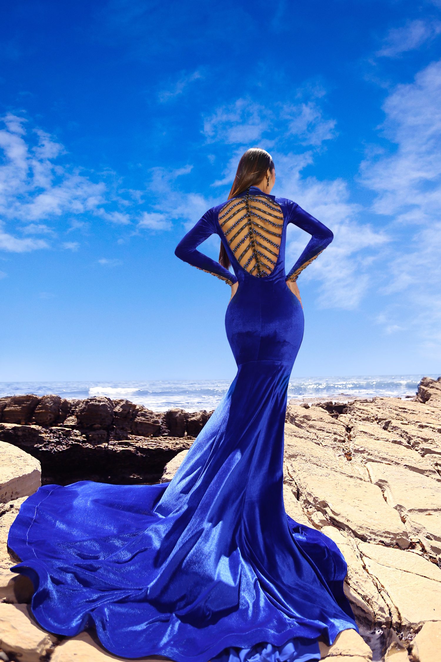 Mermaid Evening Gown Immerse yourself in the splendor of a gown, a sartorial masterpiece that contours to your figure with grace and poise. The Royal blue hue, reminiscent of the deepest ocean, exudes a regal aura, while the long, form-fitting sleeves and high collar add a touch of noble elegance. The gown’s silhouette, inspired by the mythical mermaid, flares at the hem, promising a dramatic entrance at any soirée. Stretch Velvet & Knit Fabric The fusion of the velvet and fabric ensures a fit that is both comfortable and flattering. The velvet provides a plush texture that glides over the skin, while the knit offers flexibility, accommodating every curve with ease. This blend of materials not only enhances the gown’s aesthetic appeal but also its wearability, allowing you to move with unrestricted elegance throughout the night. Open Back An backless design serves as the focal point of this exquisite gown, offering a daring reveal that is both tasteful and enticing. The open sleeves mirror this bold statement, creating a cohesive design that is both modern and timeless. This feature adds a layer of allure to the gown, ensuring that your exit is just as memorable as your entrance. Peru by Devon Couture Crafted by the illustrious Devon couture, this gown is a testament to the brand’s commitment to luxury and attention to detail. Each bead is meticulously placed by hand, creating a tapestry of shimmering embellishments that catch the light with every movement. Devon’s signature style is evident in the gown’s opulent charm, making it a coveted piece for those who seek the pinnacle of evening wear. In this stunning creation, you are not merely attending an event; you are defining it. The mermaid evening gown from Devon couture, with its luxurious stretch velvet and knit fabric, and the alluring open back, is more than just a dress—it’s a declaration of your presence. As you glide through the crowd, the gown whispers stories of elegance and grandeur, leaving a trail of captivated hearts in your wake. Embrace the night with the confidence that comes from wearing a piece that is the epitome of sophistication, knowing that in this gown, you are the embodiment of grace and the very essence of style. Let this mermaid gown be your armor and your crown as you navigate the evening, a true vision of modern-day royalty.